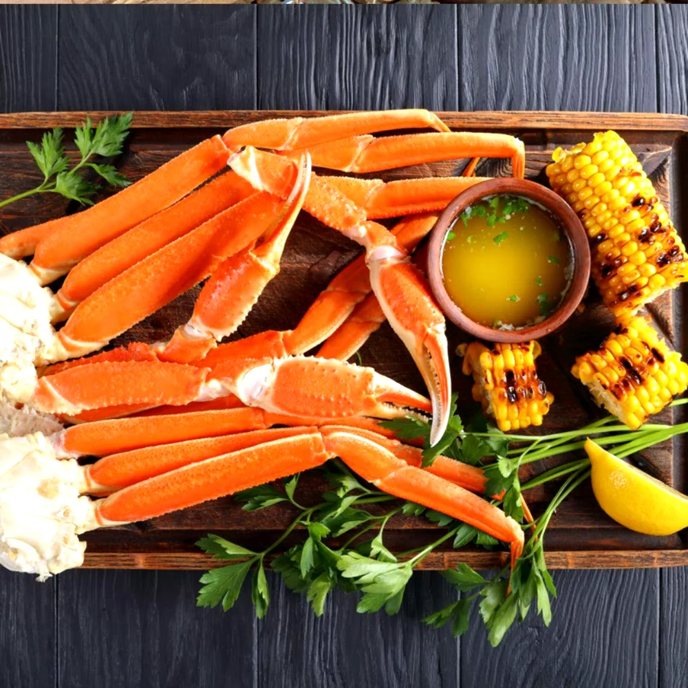 Cooked snow crab legs served with butter, corn, and lemon on wooden board